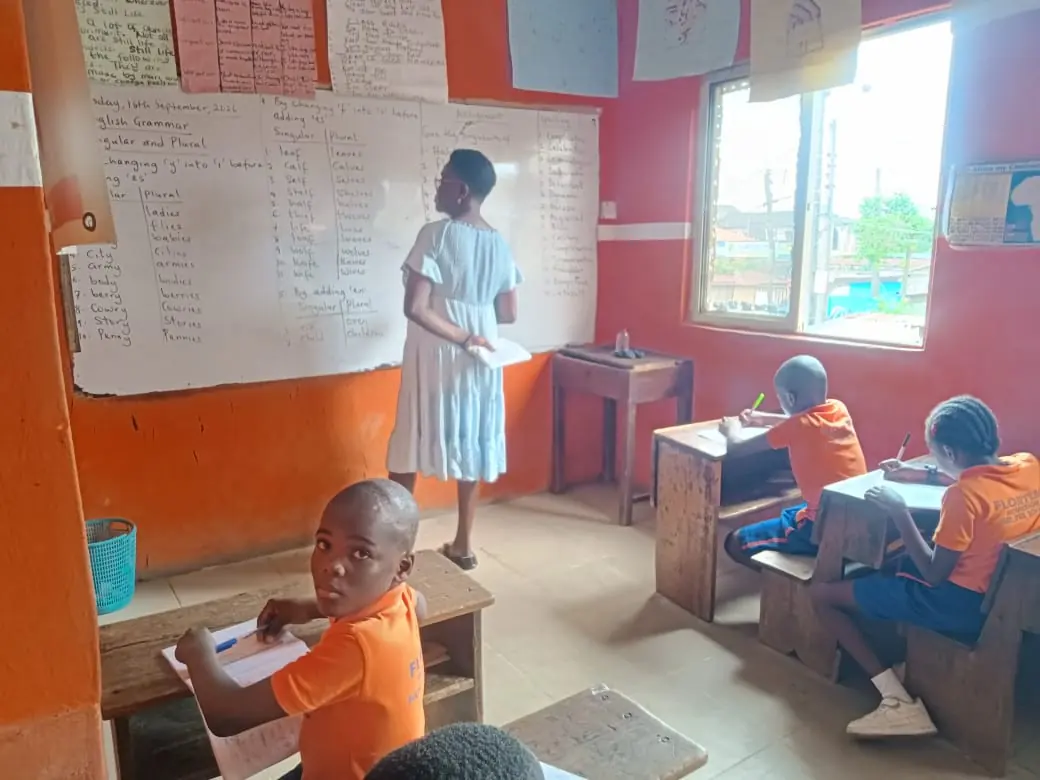 A teacher writing English grammar on the board while primary pupils write at their desks